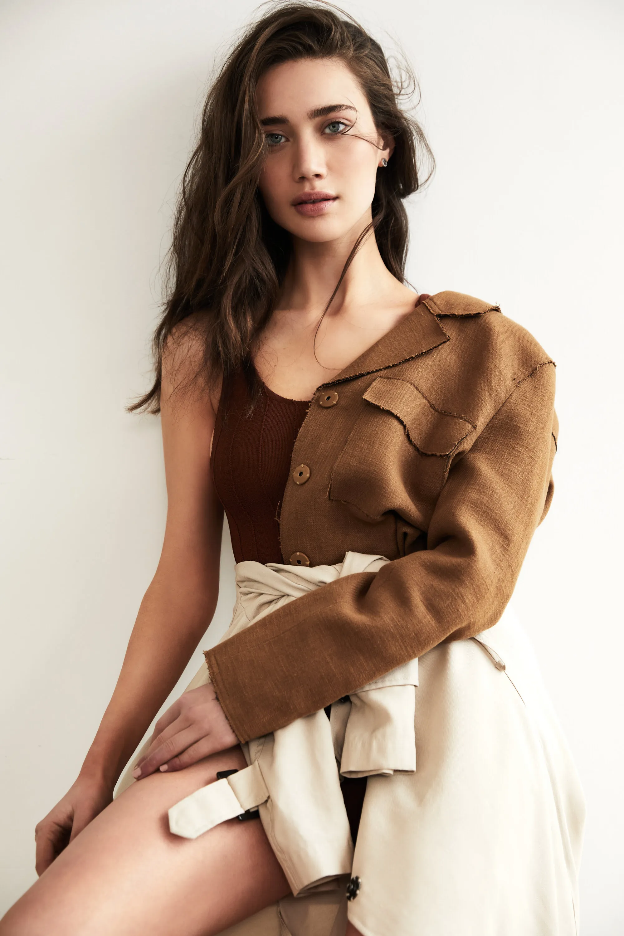 Natasha Milisic seated in brown knit layers with a cream coat tied at the waist